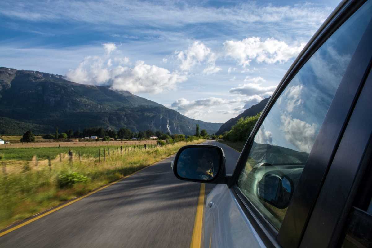 Car driving on a road with mountains in distance and clouds in sky.